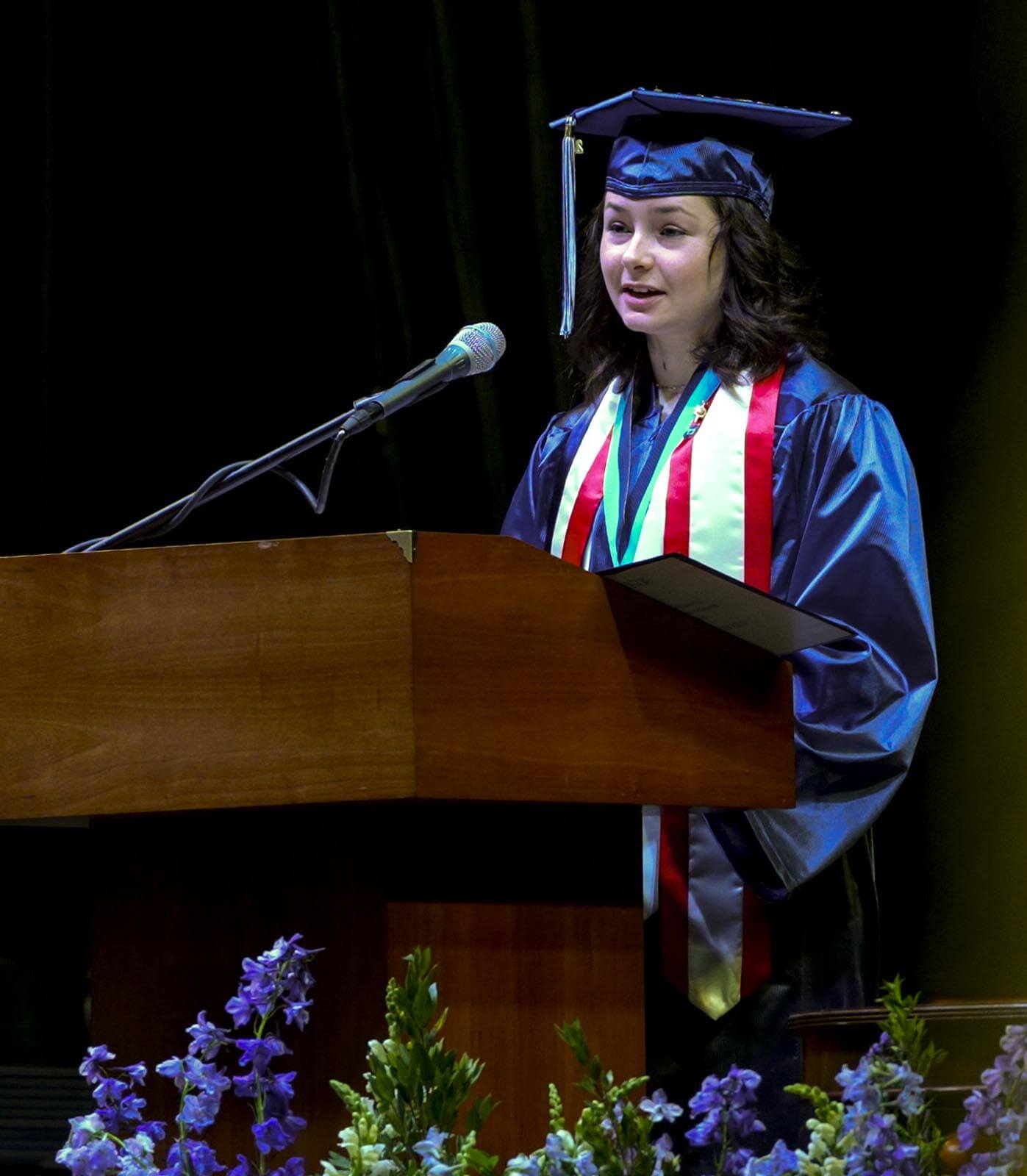 A photo of Meg Caron speaking at a podium during commencement