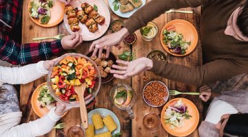 Top view of four people having dinner together while sitting at the rustic wooden table