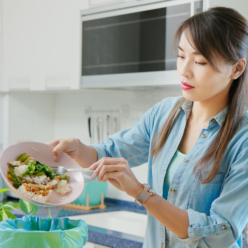 Woman scraping a plate of food into the trash