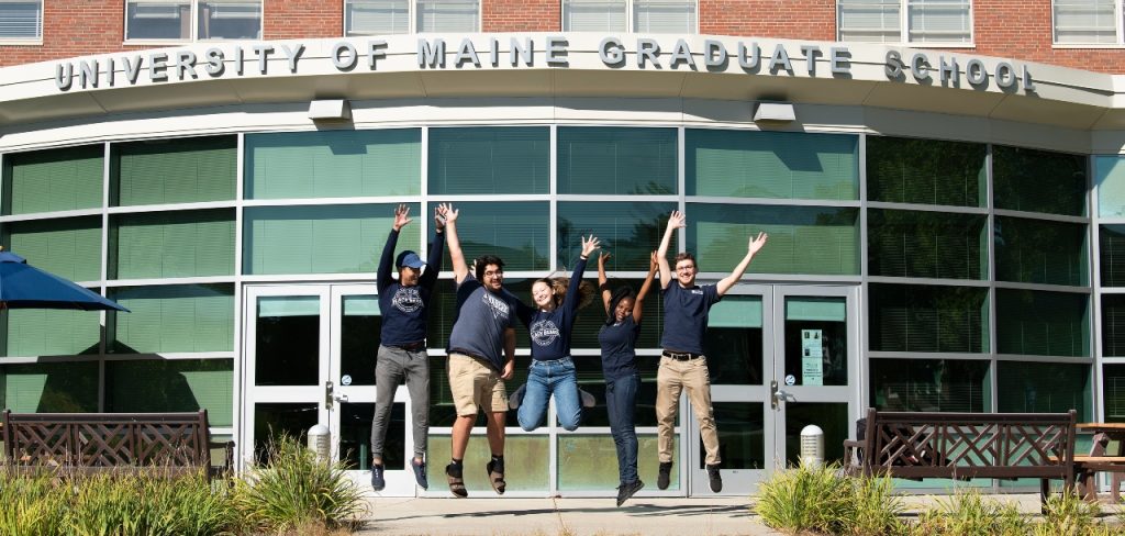 Graduate students jumping in front of UMaine's Graduate School building.