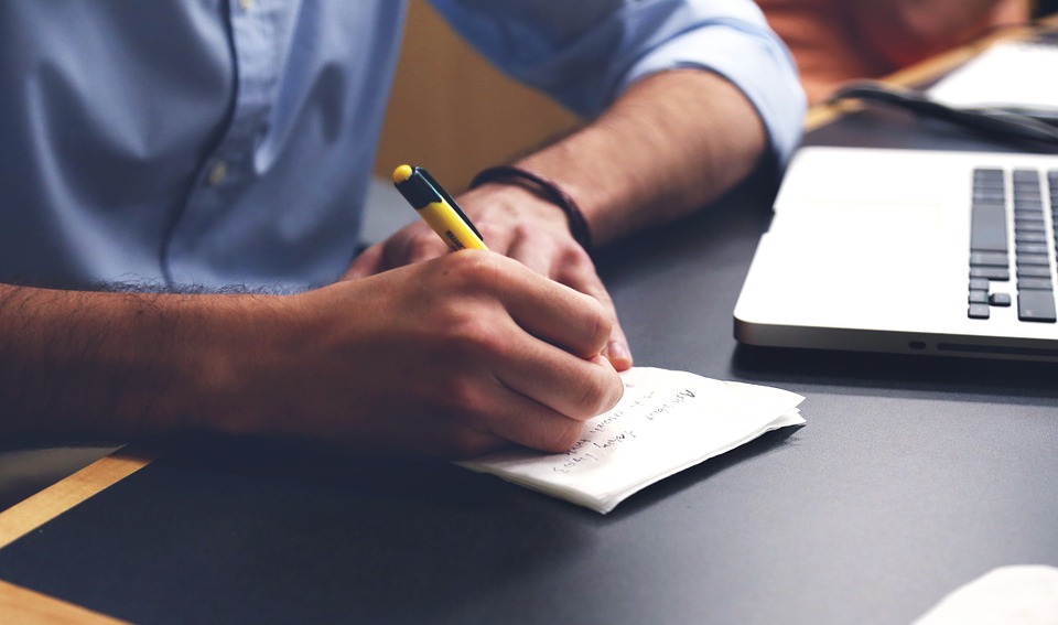 person writing at a desk next to laptop