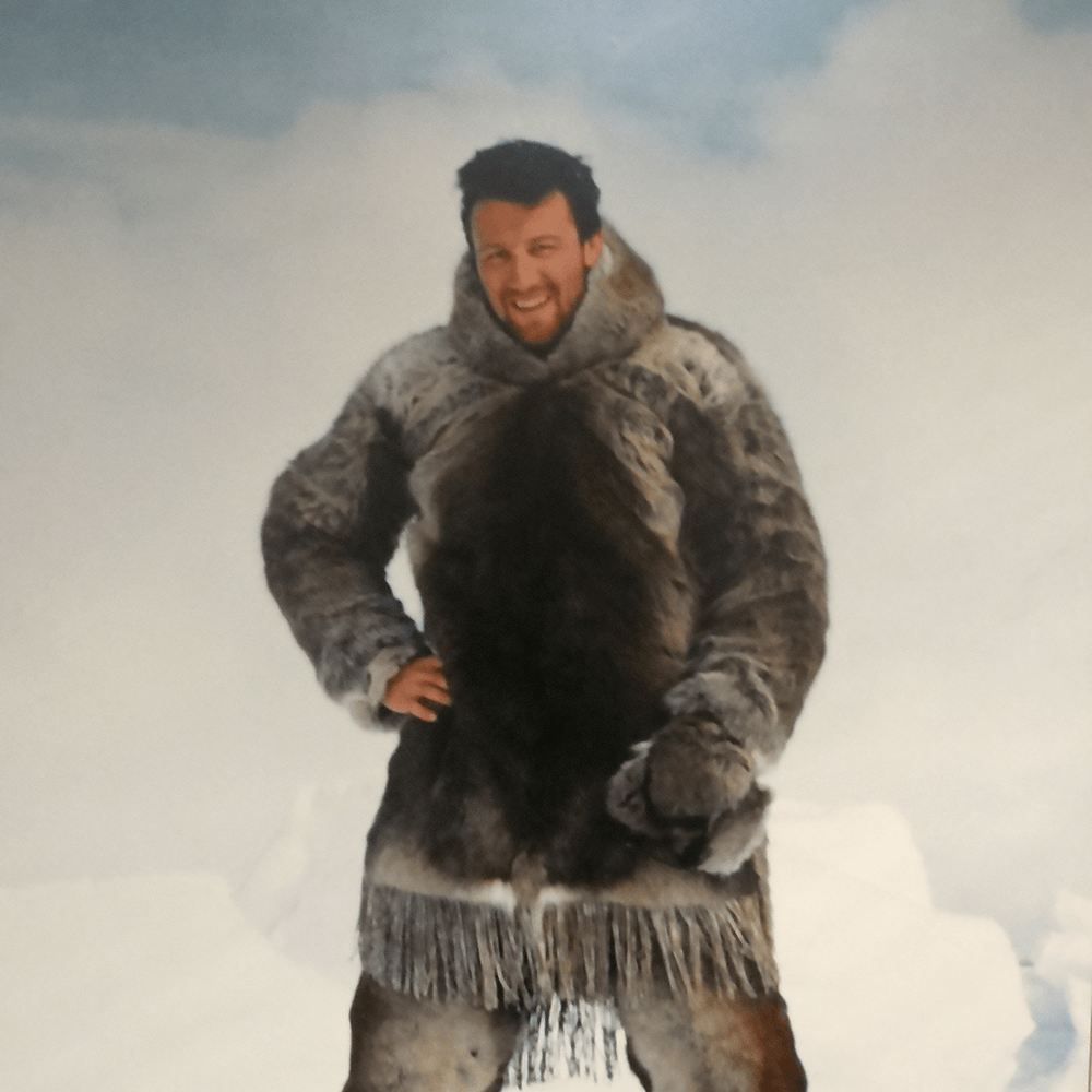 Photo of young man wearing fur outer clothes in the Arctic style and standing in a snowy landscape.