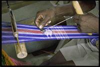 Image of a person with dark skin weaving on a simple loom.