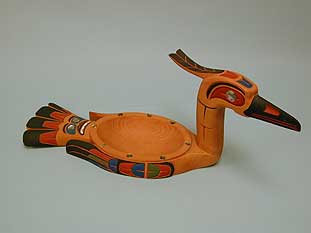 Image of a shallow wooden bowl shaped like a duck - the bowl makes up the body portion of the duck with an upright neck and head at one side, and a tail and wings around the other edges.