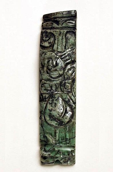 Carved greenstone object, elongated rectangular shape, incised with portions of an image of a figure sitting with crossed leg.