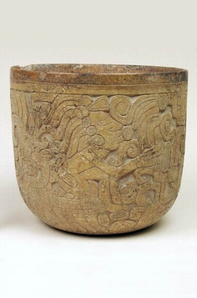 Wide vase with rounded bottom and vertical walls. Surface deeply incised with designs including a human figure with a headdress and ear ornaments. Buff colored with traces of cinnabar and red pigment and red band around rim.