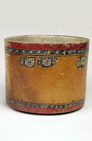 Wide vase with vertical walls painted in orange, red, black, and white. At the top, a ring of red over a black ring with white chevrons, pattern reversed at bottom of vase - chevron ring over red ring.  Pairs of glyphs beneath top chevron.