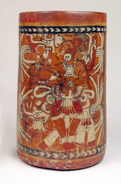 Ceramic vase, tall and narrow with vertical walls. Black and white chevron motif bands around the rim and base. A human figure with elaborate feather back rack is painted between the bands. Figure has right arm thrust forward with palm held upward.