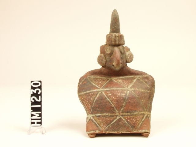 Small ceramic figure. Body is a squat rectangle with a head at center top. Ear spools and large, pointed headdress.