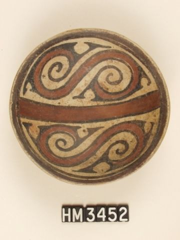 Polychrome ceramic dish. Curvilinear red design in upper and lower hemispheres represents the body of a serpent, as does the central bar, also red. Black Y-elements depicting, in profile, heads of pointy-nosed animals with curly head crests are appended to each end of the serpent bodies. Additional Y-elements may indicate the location of limbs. 