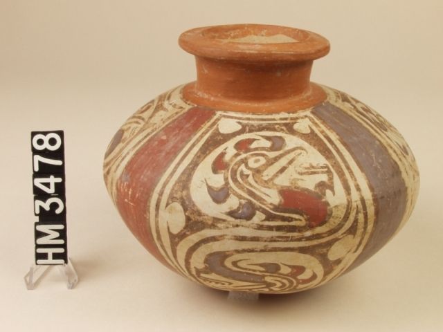 Polychrome ceramic jar with angled shoulder. A creature with bird-like beak, horizontal iguana eye slit and boa eye stripe emerges as the "tail" of the Y-element. It is enfolded within the Y-element design as a life form within a boa oval.