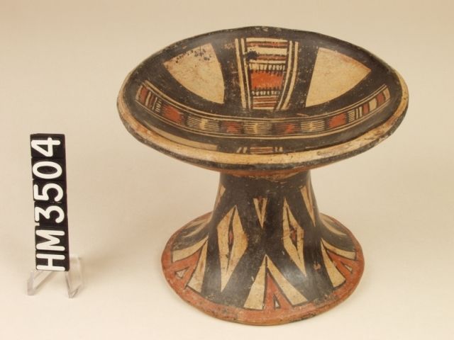 Polychrome ceramic pedestal plate. Decorated with a sequence of solid red blocks and sets of parallel lines that represent a boa constrictor.