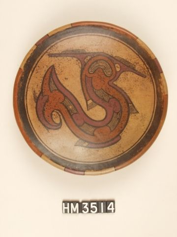 Polychrome ceramic pedestal plate. A hammerhead shark is depicted with boa markings of ovals and rectangles along its body length. Although the mouth is shark-like, its depiction also is suggestive of serpent mouth depictions. The orange color connects the mouth with the boa body line, while the red color identifies other distinctive appendages. The hammerhead, with its lobed head, appears as a "boa with appendages".