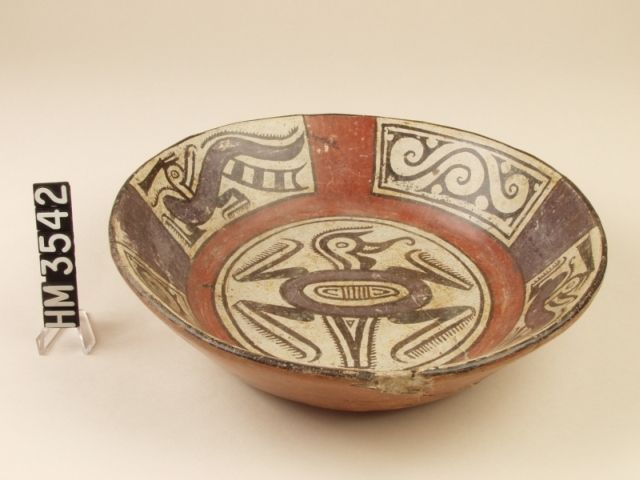 Polychrome ceramic flaring bowl with purple curassow birds on two of the side panels with barred tails, backward facing heads and head crests in the form of a severed human leg. A composite design in the center of the bowl combines avian features in the head with a quadruped with a turtle-line tail and a central red oval with red "extensions".