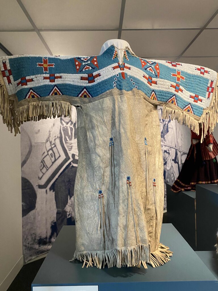 Image of a dress on an exhibit stand. It is heavily beaded along the top and both arms.