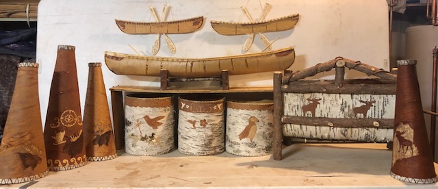Image of birchbark items on a table. Items include containers, miniature canoes, and cone-shaped moose calls.
