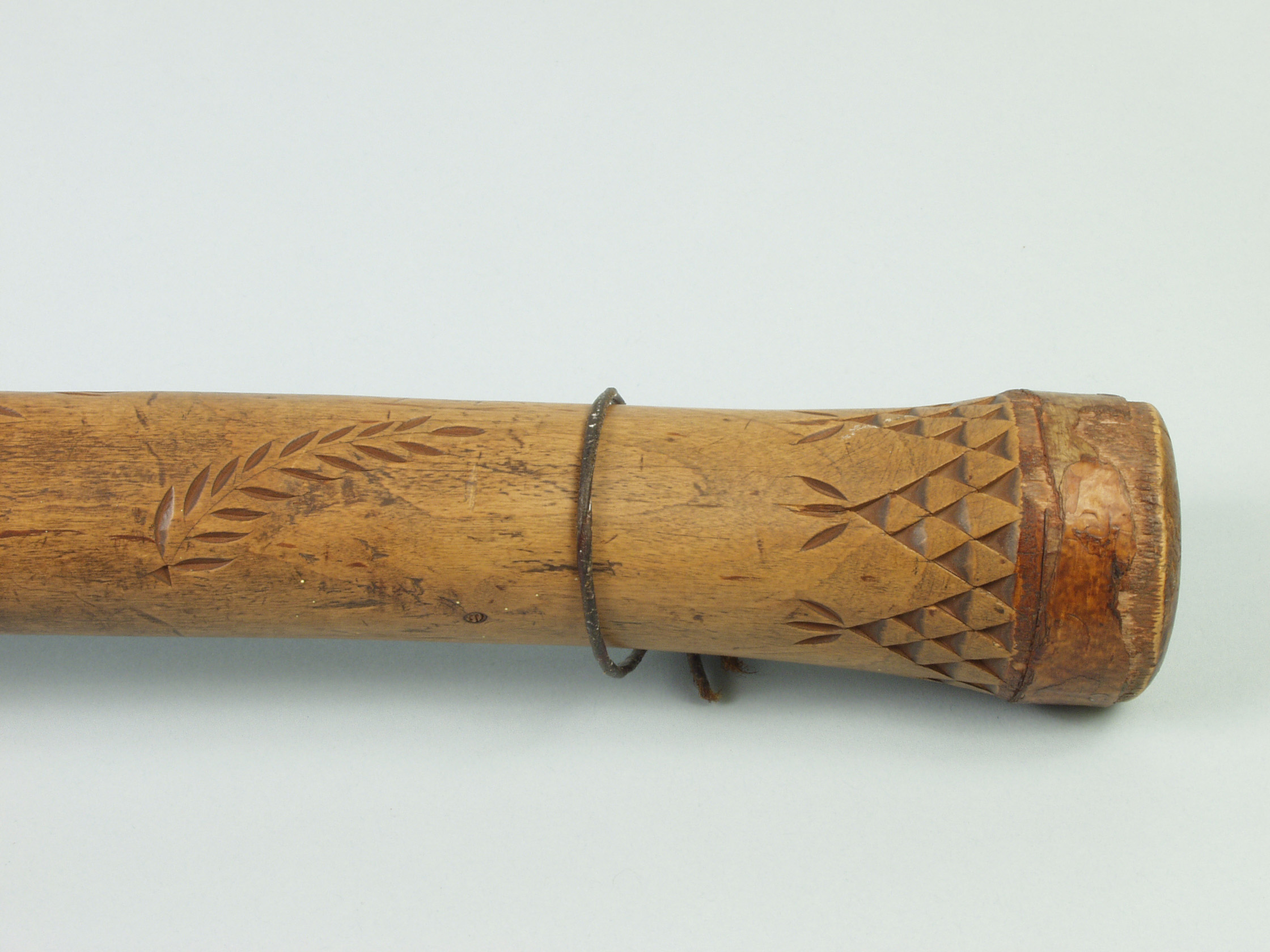 Image of the end of a wooden handle with chip-carved teepees and plant motifs.