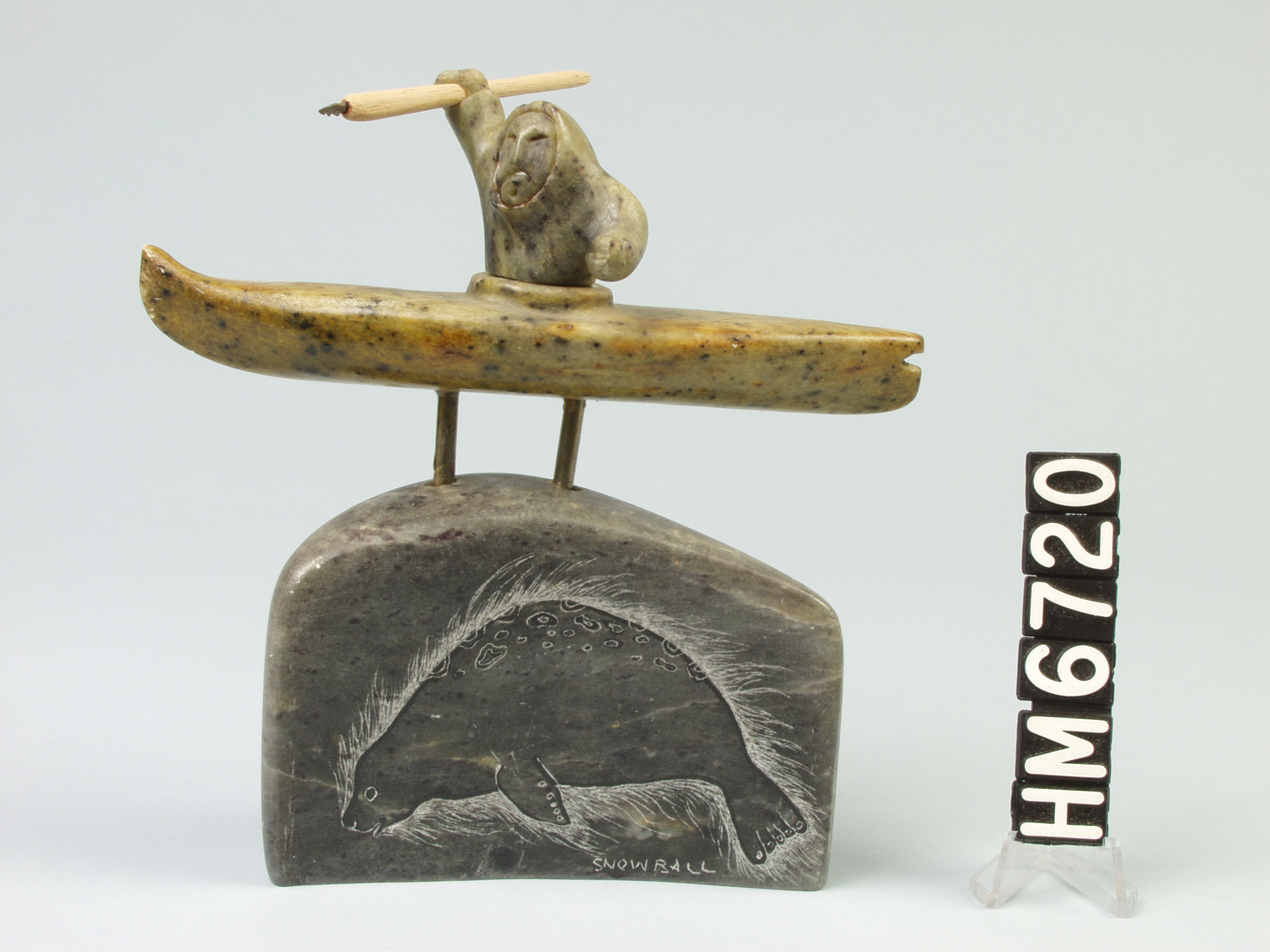 Image of a sculpture of an Inuit hunter in a kayak holding a spear above a stone base with an etched seal.