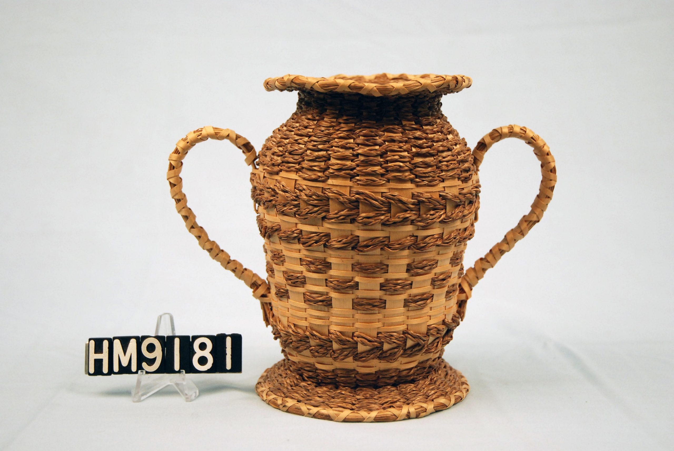 Basket in the shape of a trophy and woven around a vase.