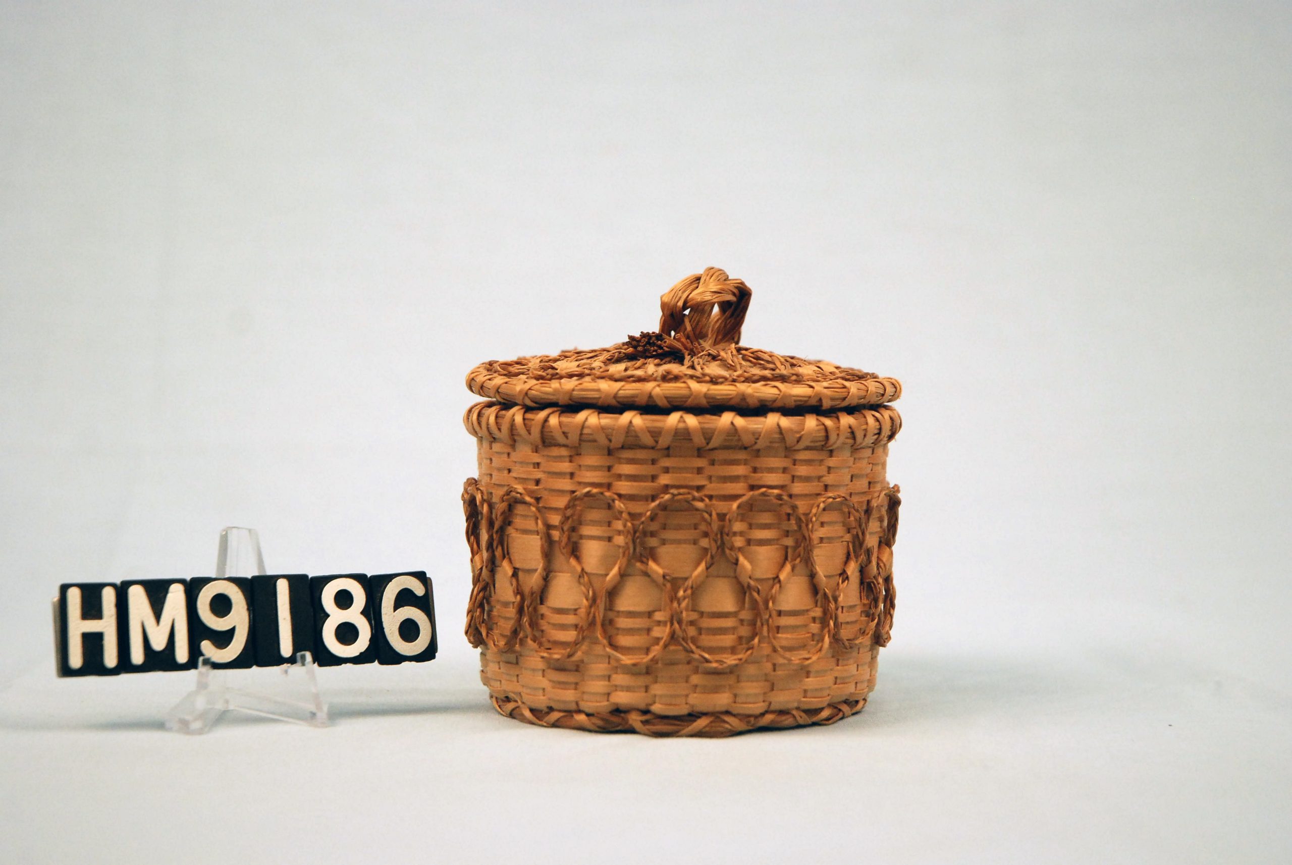 Image of small, round basket with applied details of sweetgrass braids.