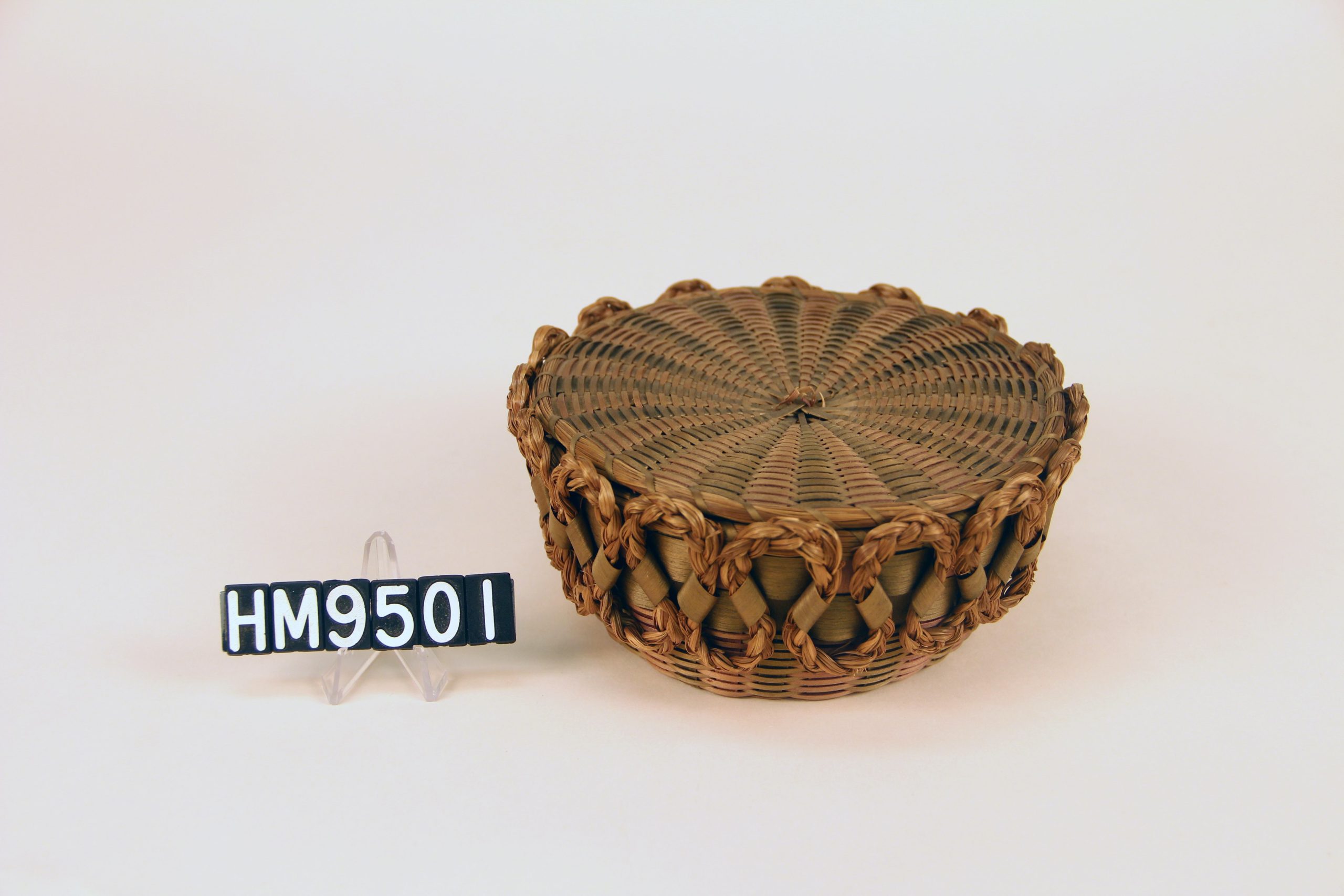 Image of round basket with decorative application of sweetgrass braid in curved forms along outer margin.