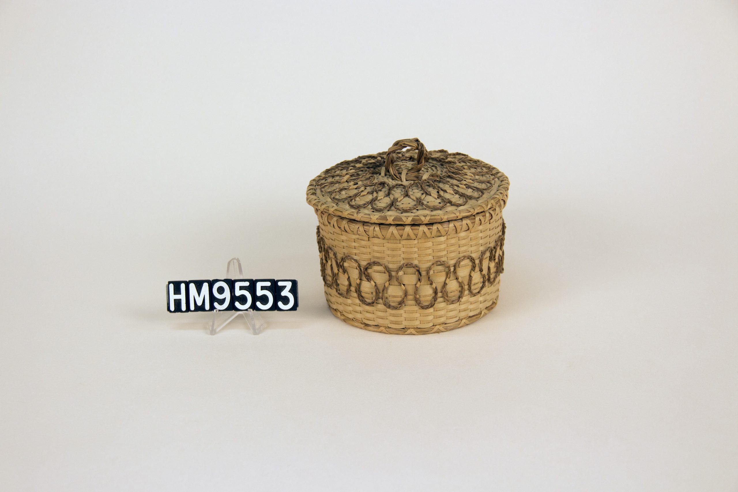 Image of small, round basket with applied details of sweetgrass braids.