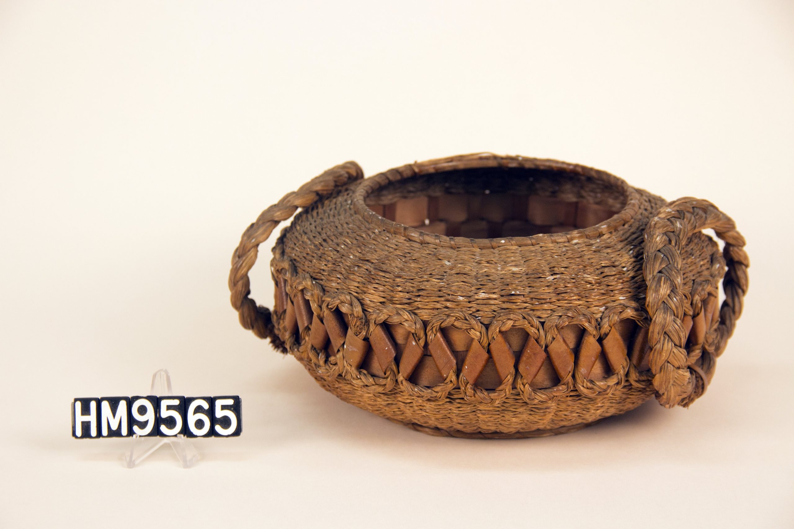 Round woven basket with flat laced sides, flat bottom and large braided side handles.