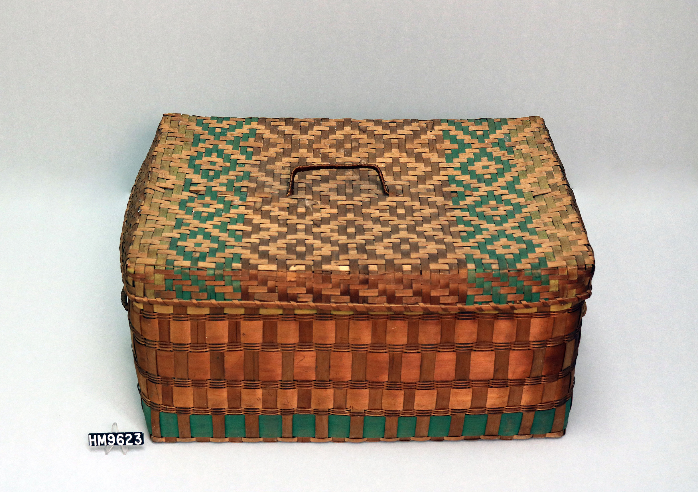 Image of large basket trunk with diamond pattern on lid and wide bands on sides.
