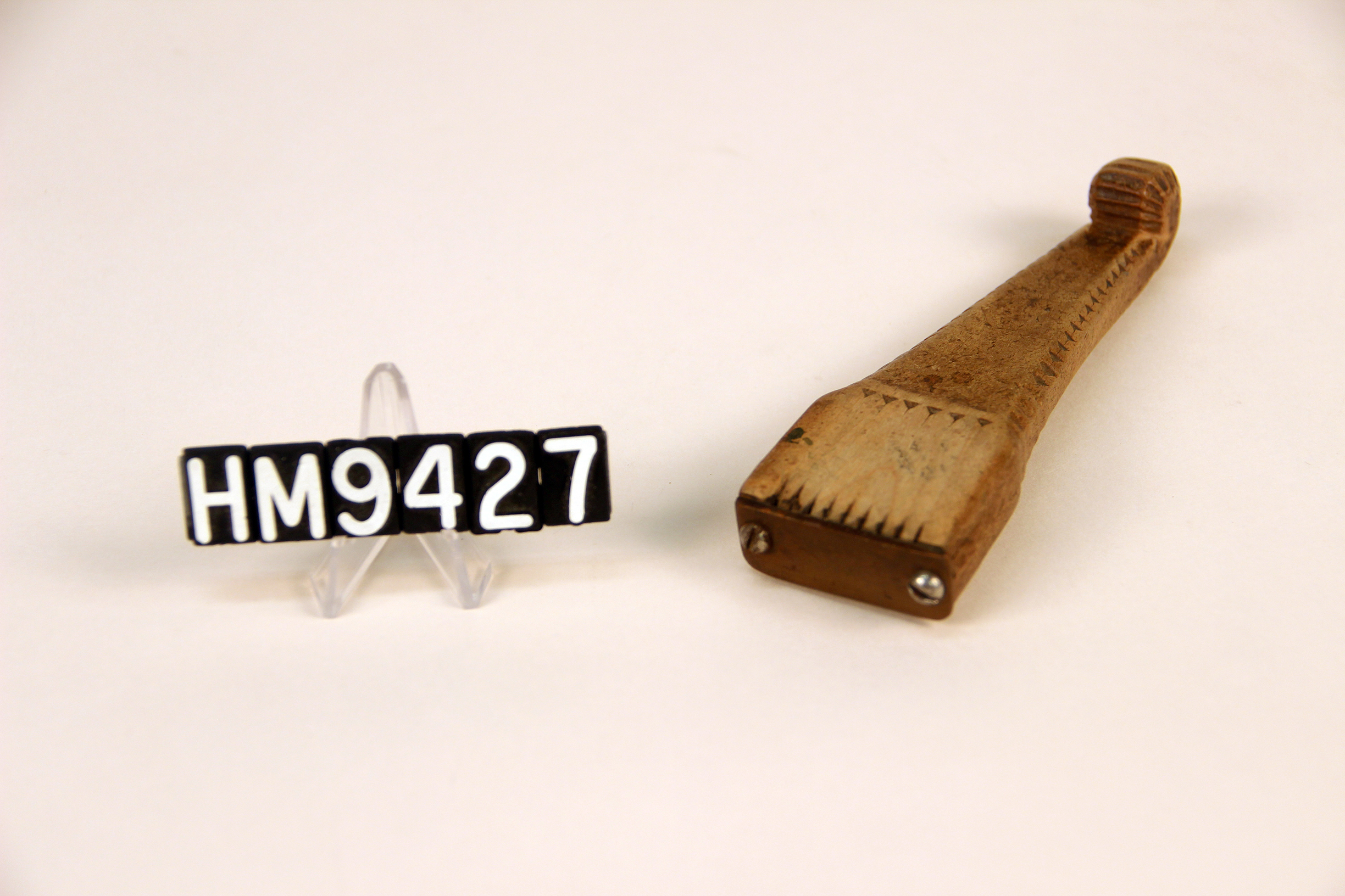Image of a wooden implement forming a handle to which thin metal teeth are attached.