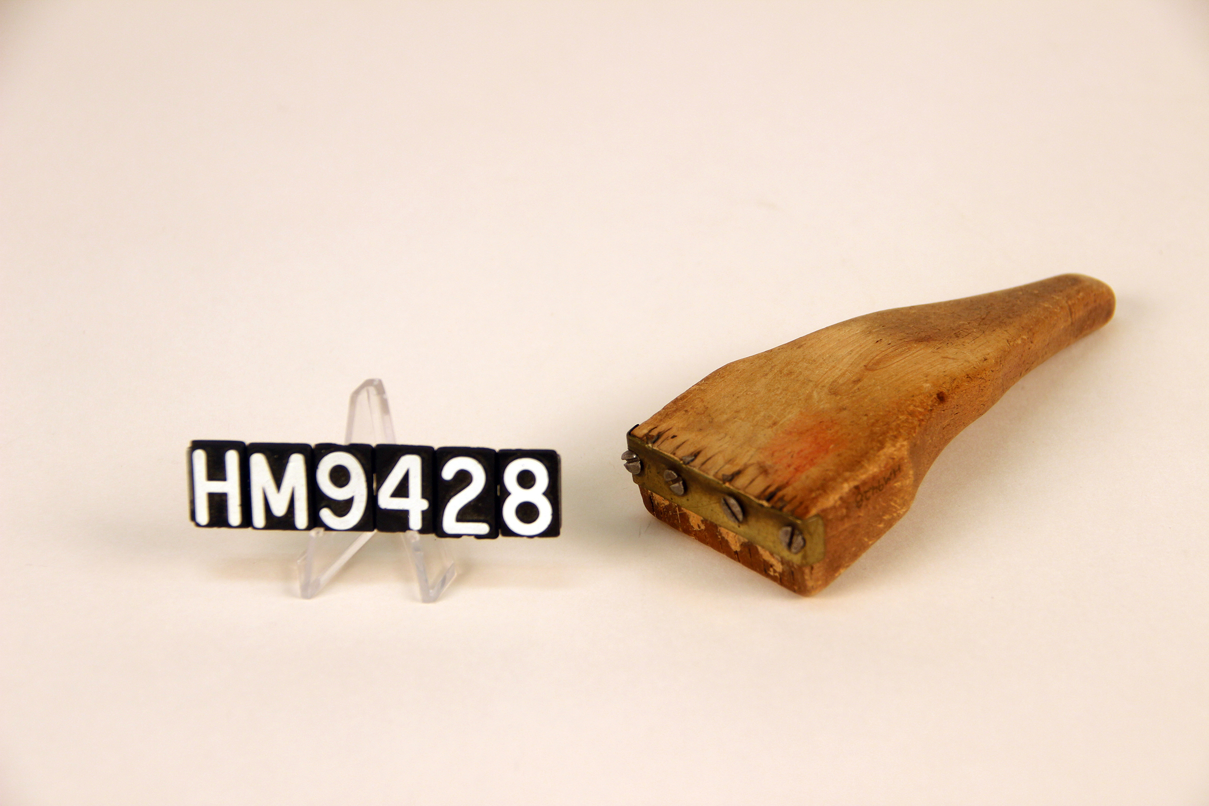 Image of a wooden implement forming a handle to which thin metal teeth are attached.