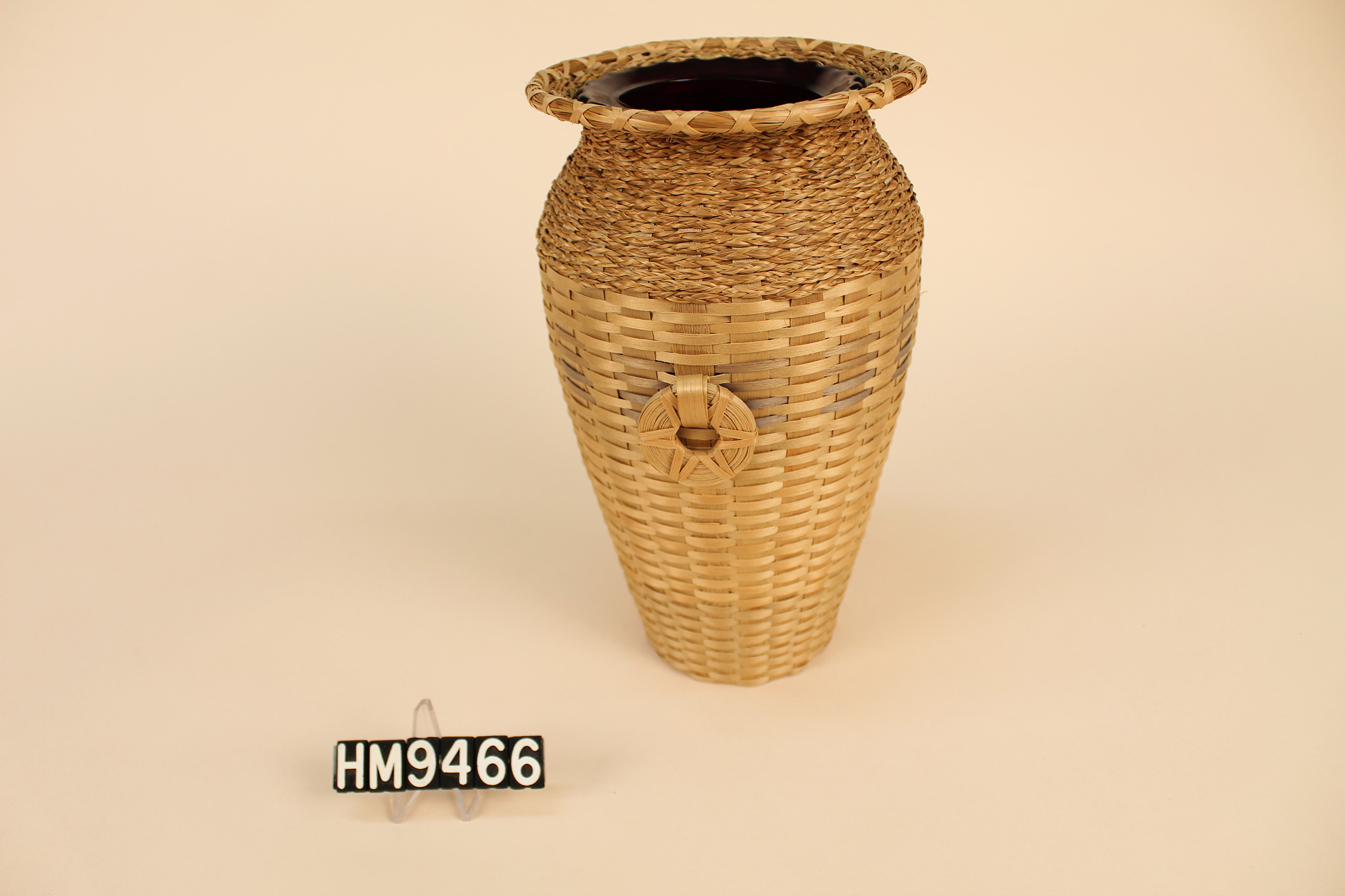 Basket woven around a glass vase with a flat, flared rim and circular handles.