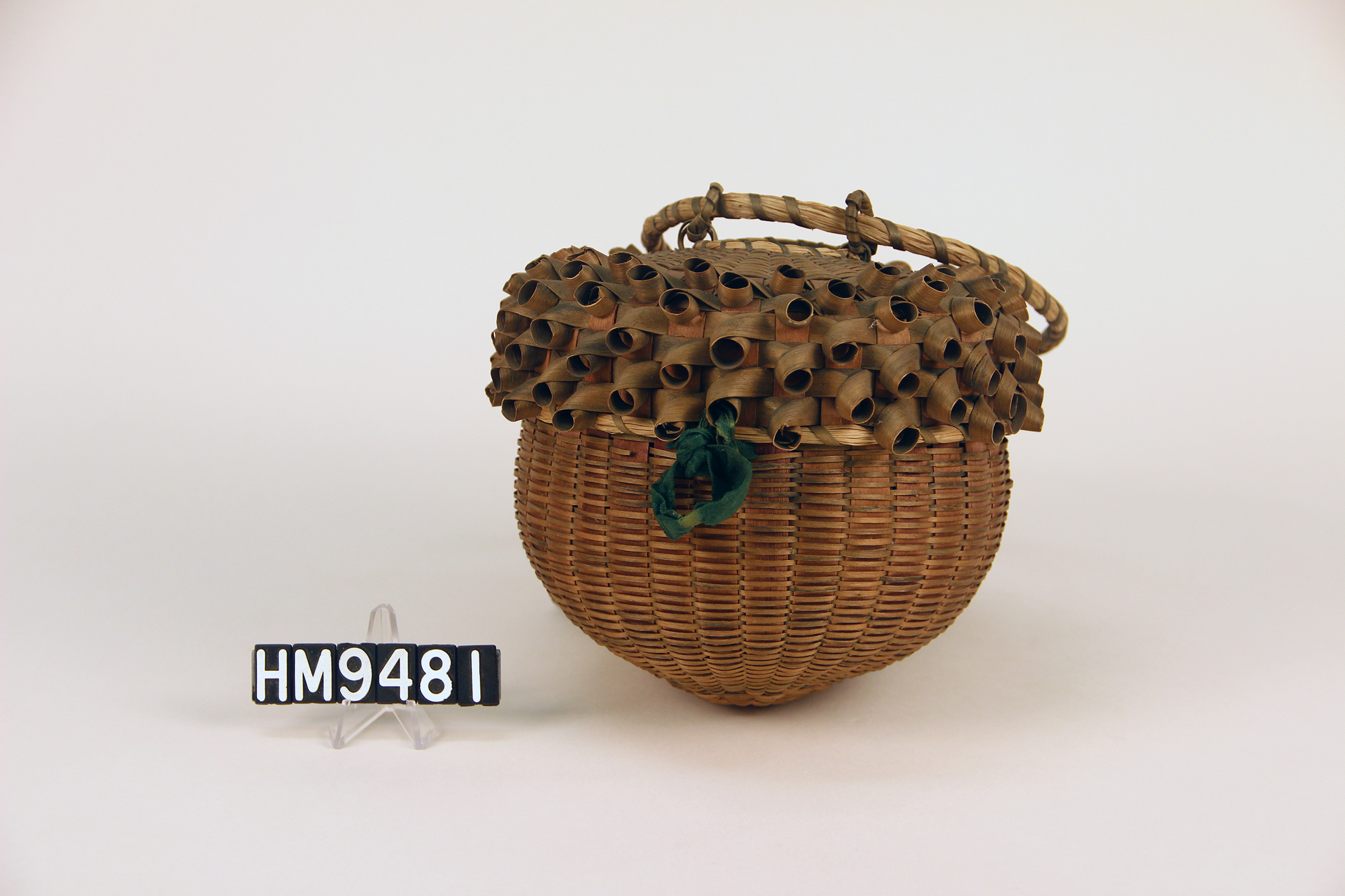 Image of a basket shaped like an acorn with curls on the cover and a green velvet ribbon closure.