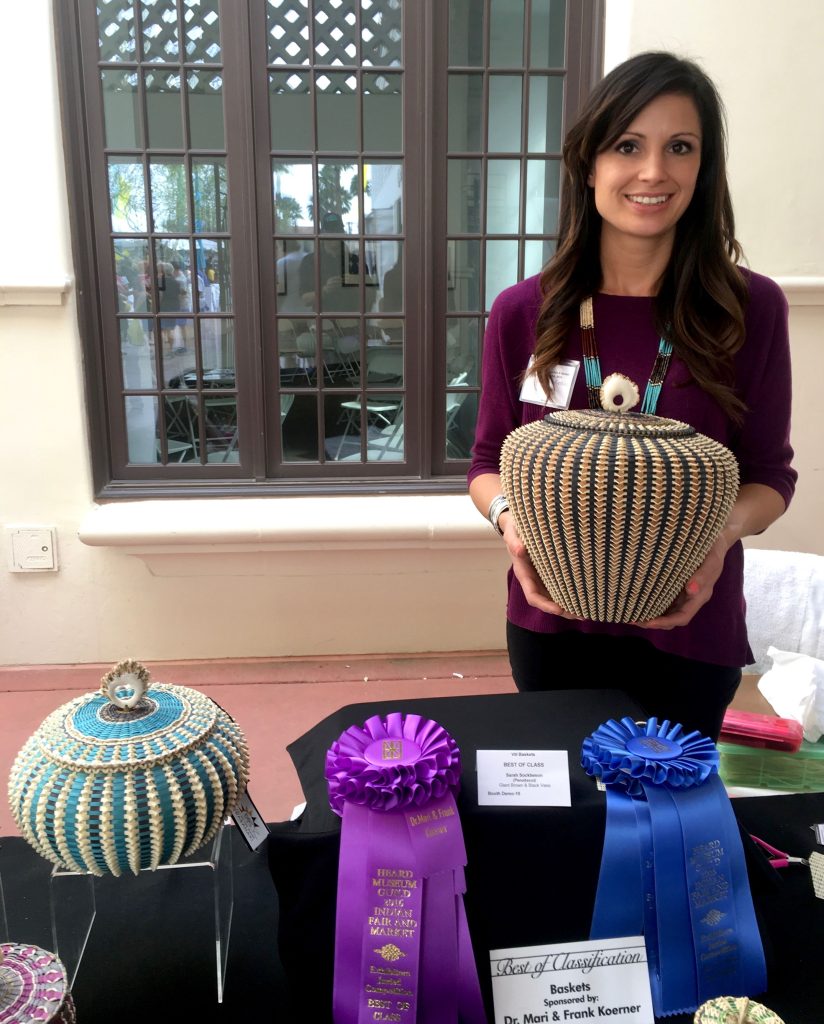 Image of woman holding ornate basket standing behind table displaying ribbons.