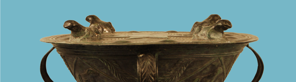 Image of the top portion of a bronze drum with strap handles and bronze frogs.