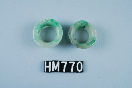 Image of two greenstone ornaments, circular in shape with open centers.