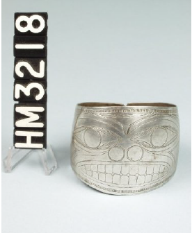 Image of a silver cuff bracelet with an incised image of a face in the Northwest Coast style.
