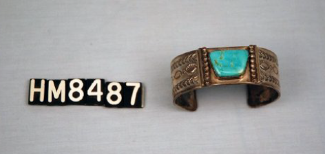 Image of a bracelet with a large turquoise set into a silver bracelet that has a deep coppery patina.