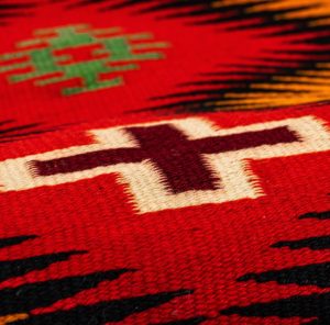 Close-up image of a woven textile. Stitches are mostly red and are very fine.