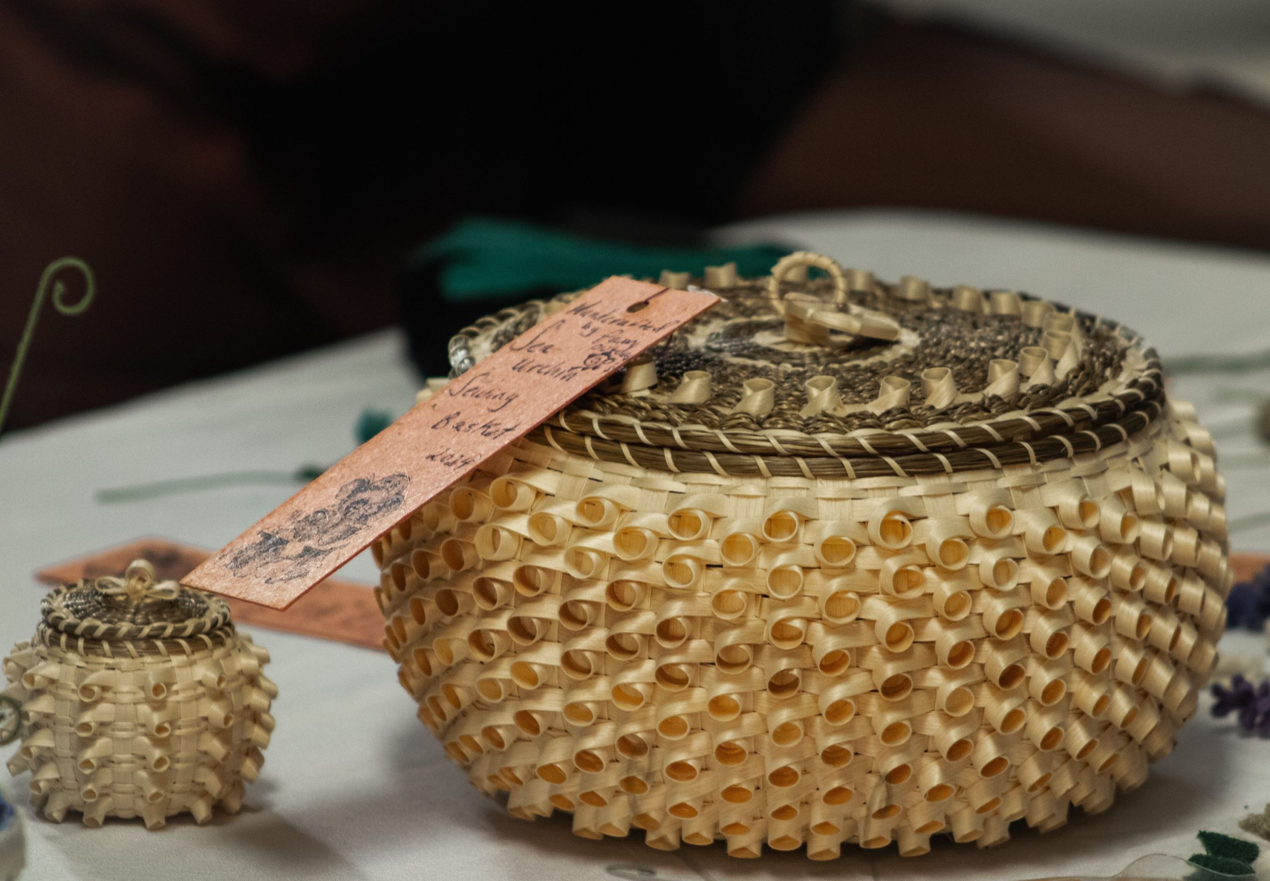 Image of two baskets sitting on a table. The larger basket has a tag attached. Both baskets are made with fancy curls.