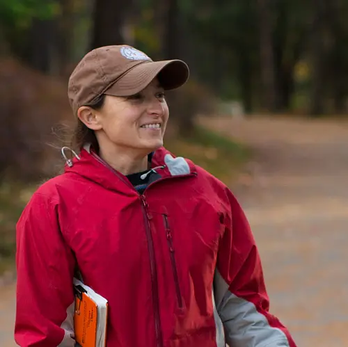 Image of Caucasian woman wearing baseball cap and red jacket looking toward right of view.