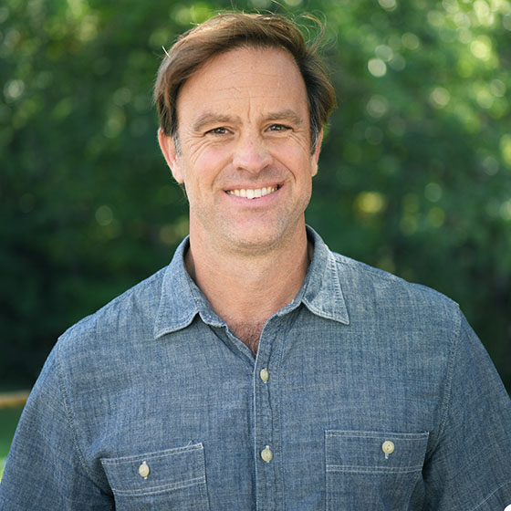 Image of Caucasian man with brown hair wearing light denim shirt outside.