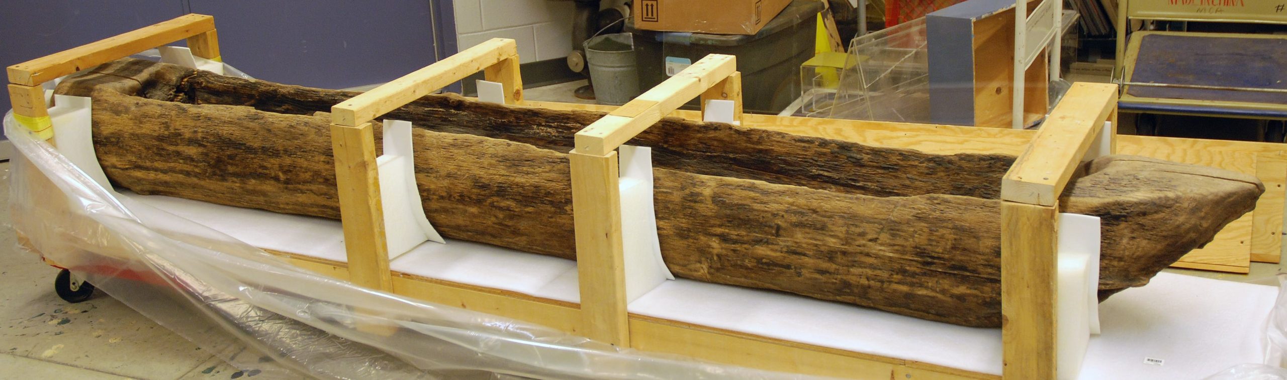 A canoe formed from a log sits within a storage housing.