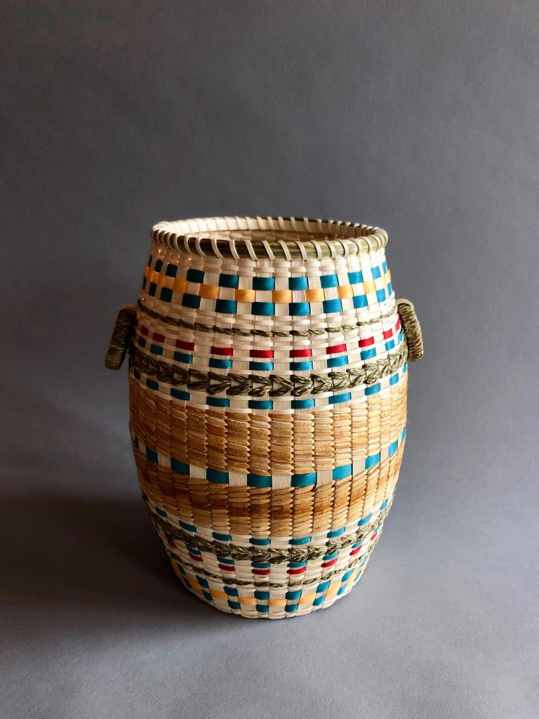 Image of a basket shaped like a barrel with details in earth tones and teal.