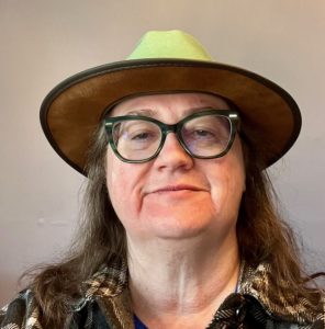 Image of Caucasian woman wearing glasses and a brimmed hat.