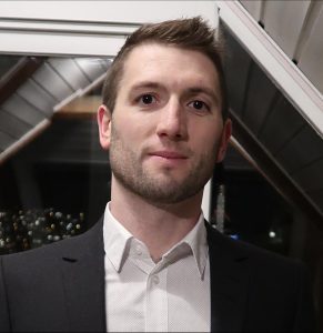 Image of Caucasian man with short hair wearing a collared shirt and jacket.