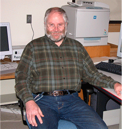 Image of Caucasian male sitting at a desk wearing jeans and a flannel