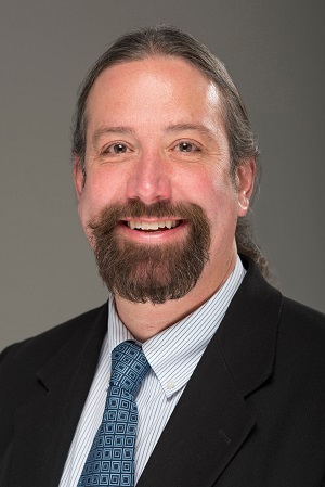 Image of smiling Caucasian man with dark hair in a pony tail, a wide goatee, and wearing a suit and tie, 