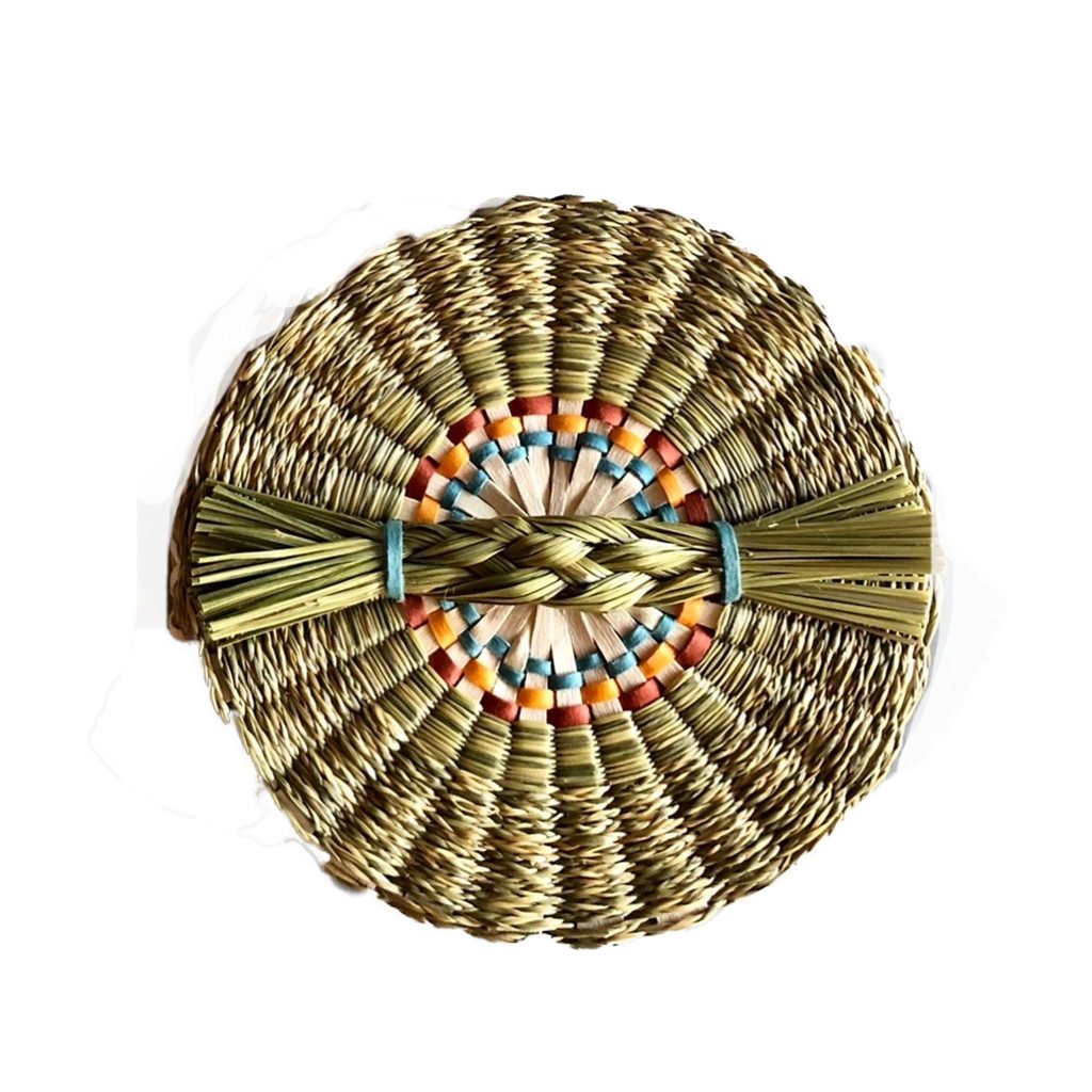 Image of the cover of a basket as seen from above. Handle of braided grass.