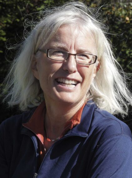 Image of Caucasian woman with pale hair and glasses, smiling, outside on a sunny day.