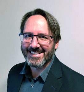 Image of Caucasian male with dark hair, glasses, and a beard wearing a collared shirt and jacket.